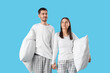 © Pixel-Shot - Young couple with pillows holding hands on blue background