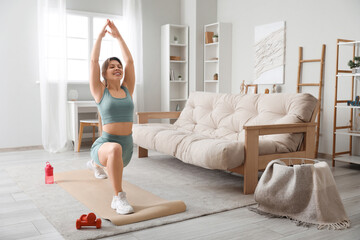 Wall Mural - Young female fitness trainer exercising on yoga mat at home