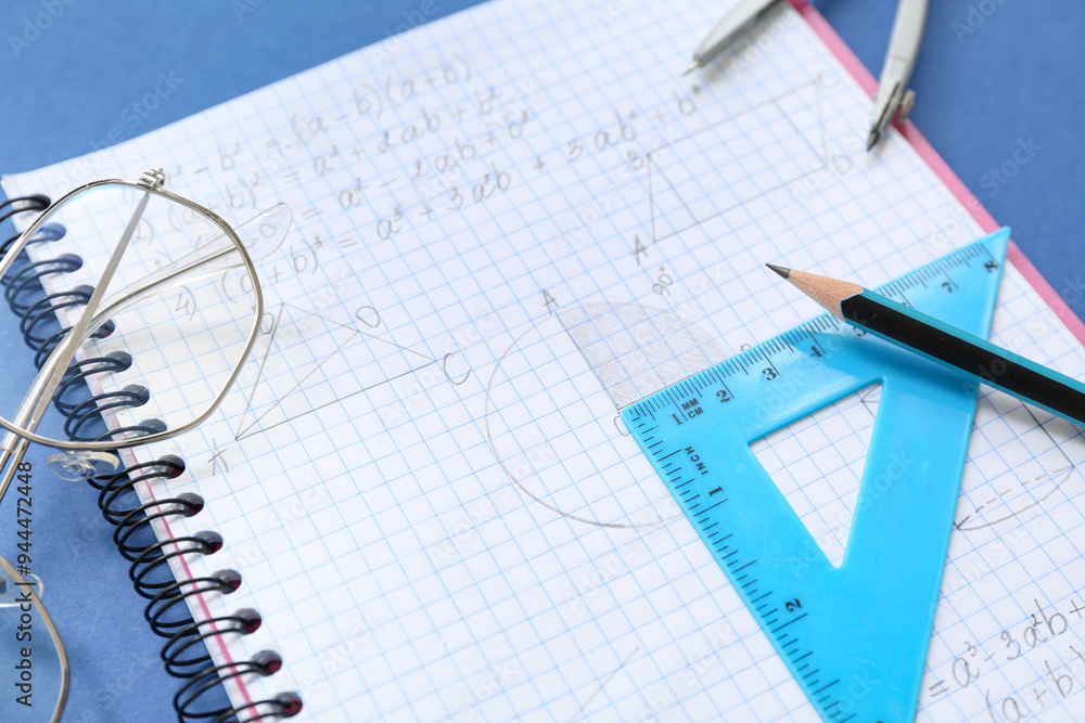 Notebook with eyeglasses and school stationery on blue background, closeup