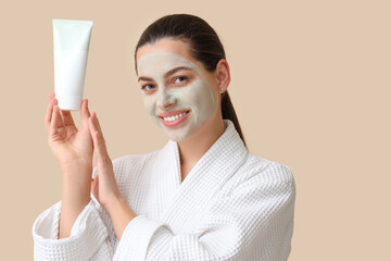 Poster - Beautiful young happy woman in bathrobe with applied clay mask on beige background