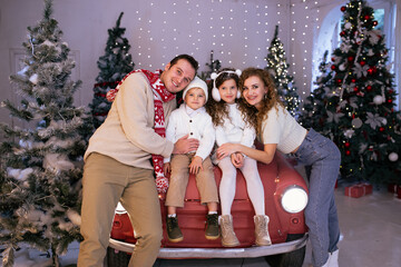 Family parents and their children having fun on Christmas time near red car and Christmas tree on background