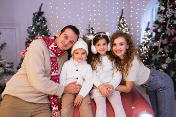 Laughing parents and their children having fun near red car and Christmas tree on background