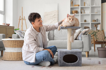 Poster - Handsome young happy man and cute Maine Coon cat lying on scratching post at home