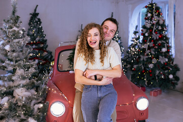 Laughing couple enjoying their time together near red car. Christmas tree on background.