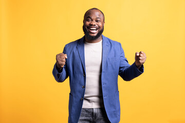 Portrait of joyful cheerful african american man celebrating, showing positive emotions. Delighted BIPOC person thrilled by achievement, cheering and gesticulating, studio background