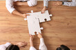 © Pixel-Shot - Business team with pieces of puzzle on brown wooden table, top view