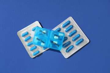 Sticker - Pill organizer and capsules on blue background. Top view