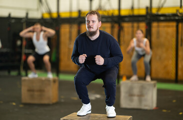 Wall Mural - Active young guy squatting on box in sports hall during crossfit workout