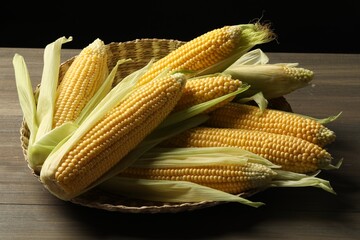 Many fresh ripe corncobs with green husks on wooden table