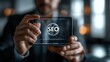 © Naret - Businessman holding transparent gadget with SEO icon. Concept of business strategy, digital marketing, and internet optimization.