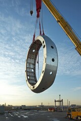 Wall Mural - The nacelle of a wind turbine is being lifted onto a tower by a crane. Nearby, other turbine components are visible
