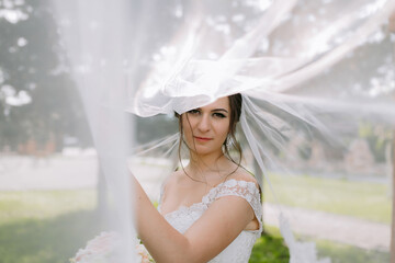 A bride is standing in front of a tree with a veil over her head. She is wearing a white dress and a veil