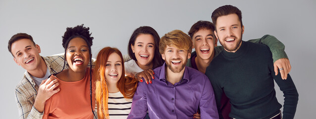 Seven happy young diverse multiracial friends having fun in photo studio. Banner with group portrait of handsome men and beautiful women in casual clothes hugging, smiling and looking at camera