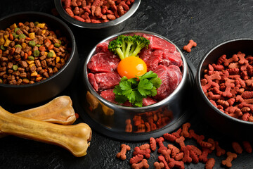 Dog bowl of fresh meat. Dry pet dog food with natural ingredients. On a black stone background.