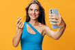© SHOTPRIME STUDIO - Stylish woman in blue top happily takes selfie with smartphone against vibrant orange backdrop