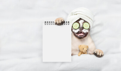 Aufkleber - Funny Pug puppy with towel on it head and with pieces of cucumber on it eyes relaxing on the bed at home and showing empty list. Top down view. Empty space for text