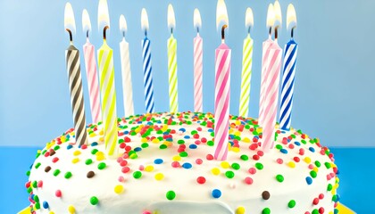 A birthday cake with a smooth white frosting, adorned with an assortment of colorful sprinkles and ten lit candles in different striped patterns.