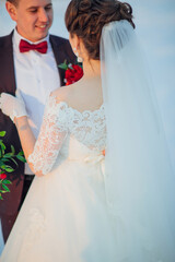 Wall Mural - A bride and groom are posing for a picture. The bride is wearing a white dress with lace detailing and a red bow. The couple is standing in front of a snowy background