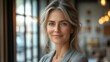 © julija - professional portrait of a confident middleaged businesswoman smiling in a modern office setting with a cityscape visible through large windows
