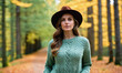 © Miklos - A woman wearing a brown hat and green sweater stands in a forest path during autumn