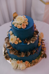 A blue cake with white flowers on it. The cake is three layers and has a gold leaf design on the bottom