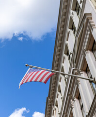 American flag on a flagpole against a blue sky and a light facade of a historic building