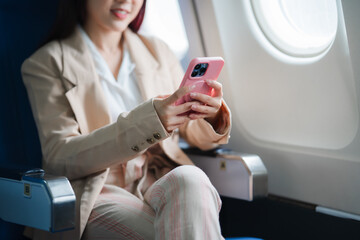 woman on airplane using smartphone: a young woman in a stylish beige blazer and pink pants, sits com