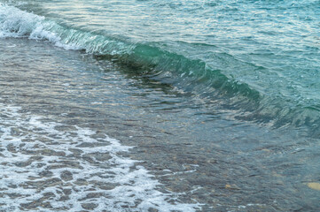 Sea waves on the pebble beach. Blue sea surface with waves. Abstract background of water flow in ocean, sea, river, lake. Seascape wallpaper.