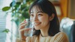 © Elkhan Babayev - Asian woman relaxes at home, drinks water, smiles, and looks away. She feels cheerful and healthy.