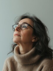 Aufkleber - A woman with glasses sits thoughtfully, looking up with a serene expression. Soft light highlights her features and the cozy atmosphere around her. Generative AI
