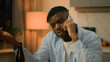 © Yuliia - Drunk alcoholism addicted African American man guy male drinking alcohol drink beer at home evening talking mobile phone call smartphone talk speak suffering problem trouble sad upset stress depress