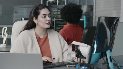 Wall Mural - waist up slowmo of middle eastern woman holding vr headset in hand while using desktop computer, wor
