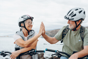 Canvas Print - Couple of two seniors giving five together outdoors having fun with bicycles enjoying nature. Couple of old people building a healthy and fit lifestyle..