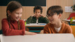 © Yuliia - Two Caucasian children school lesson girl boy classmates laughing talk evil laugh mocking bully African American kid child schoolboy sad upset stressed lonely mock bullying kids class discrimination