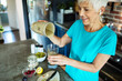 © Marko Geber - Smiling senior woman pouring healthy smoothie in glass at kitchen