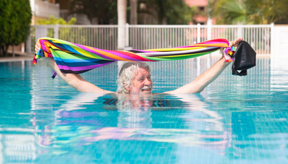 Wall Mural - Senior white haired man getting out of outdoor swimming pool holding towel, swimming cap and goggles. Caucasian retired man enjoying healthy and active life