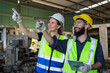 © eakgrungenerd - Supervisor engineer and operational level employees wear helmet in uniform holding tablet working together at machine lathe metal heavy industrial.
