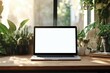 © lunarts_studio - A blank screen laptop rests on a wooden desk, flanked by potted plants and office supplies. This well-lit workspace promotes creativity and productivity in a natural environment