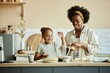© Seventyfour - Smiling African American girl and young mother making banana smoothie on large counter having fun and sharing happy moments at cozy beige kitchen, copy space