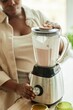 © Seventyfour - Cropped shot of Black woman using kitchen blender mixing ingredients making milk smoothie on beige wooden counter, copy space