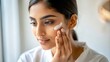 © N7 - Close-up of an Indian woman gently applying face cream, emphasizing skincare.