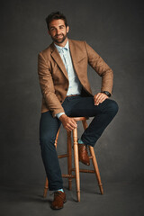 Poster - Portrait, chair and business man in studio with trendy style, accessory and formal clothes. Professional fashion, happy entrepreneur and person with confidence, pride and smile on gray background