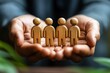 © Worrapol - Protecting Our People: Four wooden figures cradled securely in open hands, symbolizing the importance of human resources, teamwork, and care within a business or organizational context.