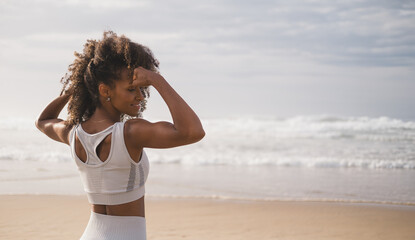 back view of fit black woman flexing arms towards the sea at the beach. fitness motivation and succe