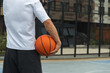 © svetlana_cherruty - Sporty man holding orange basketball ball on sports court. Basketball Hoop. View from back. Urban city park outside. Close up.