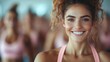 ©  Shomixer - A close-up photo of a young woman in pink fitness attire smiling cheerfully in a fitness studio, illustrating a happy and energetic atmosphere with other fitness enthusiasts in the background.