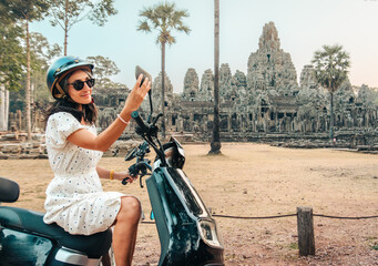 Happy young caucasian tourist driver with electric scooter stand by famous Angkor wat historical site temples - Angkor Thom. Travel explore south-east asia with rented scooter concept