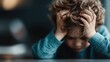 ©  Shomixer - A young child with curly hair holds their head in their hands, possibly feeling overwhelmed or stressed, as they sit at a table in a contemplative pose.