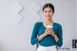 © David - Young successful employee business asian woman in blue shirt work hold takeaway delivery craft paper cup coffee to go stand at desk with laptop pc computer at office.