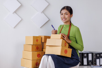 Wall Mural - SME business asian entrepreneurs small in Asia Write shipping information on a cardboard box in home office. Small business sme operators preparing to ship to customer